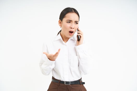Angry business woman shouts at mobile phone, has intense conversation on telephone, stands over white background photo