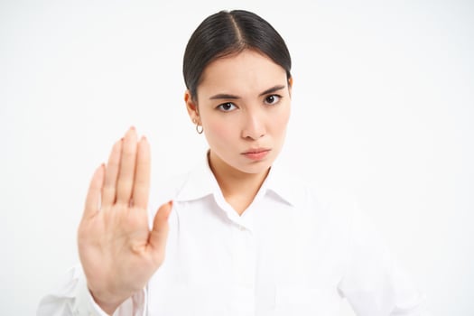Please stop, enough. Serious asian female manager, businesswoman shows extended hand gesture, disapproves, prohibits smth, white background photo