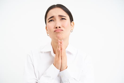 Upset asian woman looks up with desperate and sad face, complains to Lord, stands over white background photo