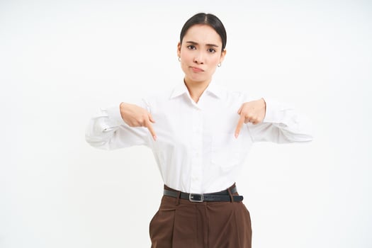 Disappointed lady boss, young woman points down with concerned, frowning face expression, white background photo