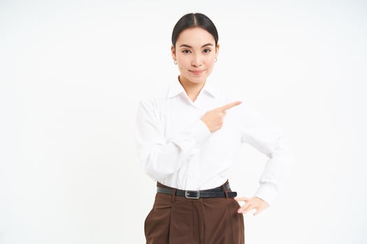 Business. Corporate asian woman points finger right, shows advertisement, banner promo, stands over white background photo