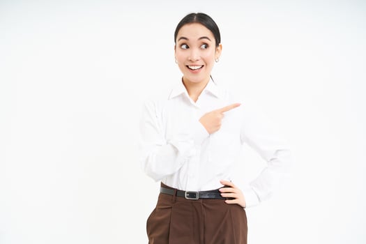 Business. Corporate asian woman points finger right, shows advertisement, banner promo, stands over white background photo