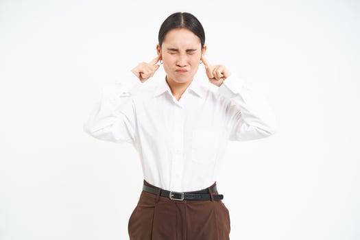 Frustrated young woman, shuts ears with fingers and grimaces from discomfort, annoyed by loud noises, white background photo