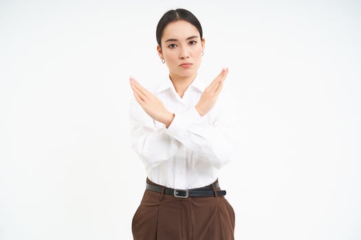 Stop sign. Young serious businesswoman shows cross sign, rejection, prohibit something, standing over white background photo