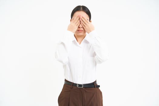 Portrait of young asian woman covers her eyes with hands, hides from something, white background photo