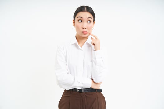 Thoughtful asian woman, businesswoman scratches her face and thinks, makes decision, white background photo