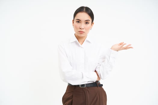 Professional businesswoman, looks puzzled at camera, extends one hand with confused face expression, white background photo