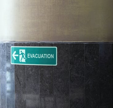 Selective fire exit sign on white ceiling. Green fire escape sign hanging on office wall. Fire fighting equipment concept. photo