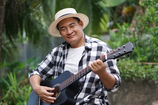 Handsome Asian man is playing acoustic guitar in the park, outdoor nature background. Concept, love music, hobby, recreation activity. Relax time. Music can develop mental health. photo