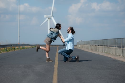 On the road, a young couple proposes to each other, with wind turbines in the background. photo