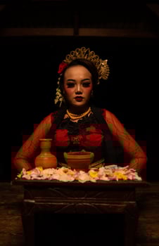 An Asian woman in a red dancer's dress is sitting at a ritual offering table full of flowers photo