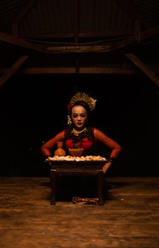 An Asian woman in a red dancer's dress is sitting at a ritual offering table full of flowers photo