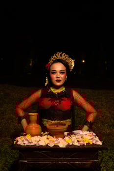 Close up shot of an Asian girl in red clothes sitting on her knees in front of a flower offering photo
