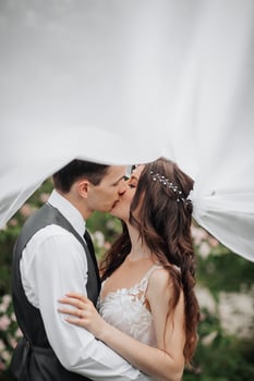 Happy young couple. Wedding portrait. The bride and groom tenderly kiss under a veil against the background of a blooming bush. Wedding bouquet. Spring wedding photo