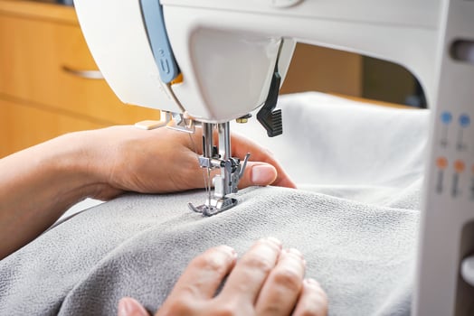Female hands stitching gray fabric on modern sewing machine. Close up view of sewing process. photo