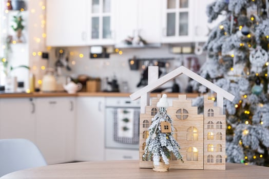 Key on Christmas tree and tiny house on cozy home with Christmas decor on table of festive white kitchen. Gift for New Year. Insurance, moving to new house, mortgage, rent and purchase real estate photo