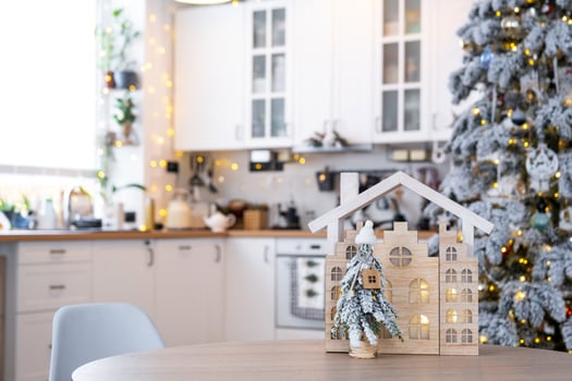 Key on Christmas tree and tiny house on cozy home with Christmas decor on table of festive white kitchen. Gift for New Year. Insurance, moving to new house, mortgage, rent and purchase real estate photo