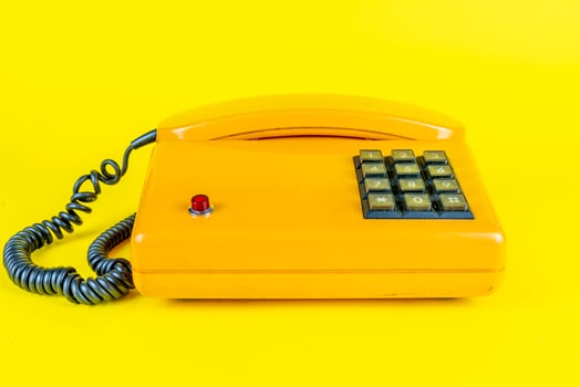 yellow plastic vintage telephone with red button on a yellow background photo