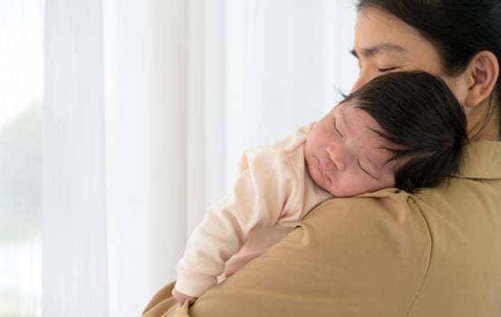 Cute newborn baby girl sleeping on mother shoulder near window at home photo