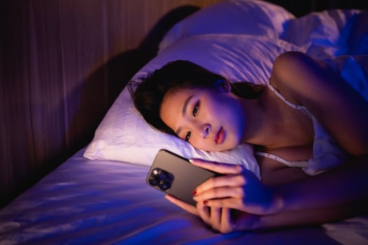 Asian woman using mobile phone smartphone laying on the bed in the bedroom. Sleepy exhausted, can not sleep. Insomnia, addiction concept. Women scrolling social networks on mobile dark bedroom. photo
