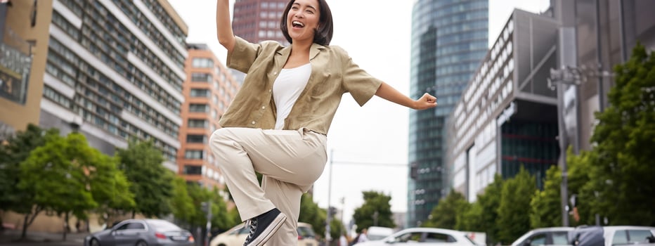 Portrait of dancing asian woman, raising hands up and feeling happy, posing in city, triumphing, feeling joy photo
