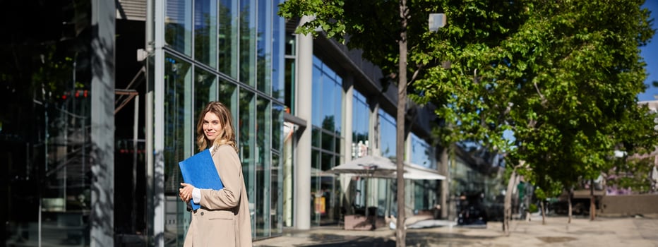 Portrait of businesswoman in beige suit and high heels walking on street. Corporate woman going to work, holding folder with documents photo