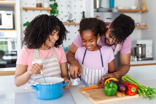 Cute little girl and her beautiful parents are cutting vegetables and smiling while cooking in kitchen at home photo