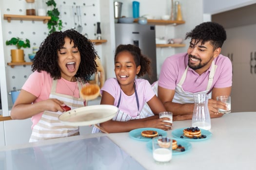 Smiling mother tossing pancakes as she shows off to her young daughter as they prepare breakfast with father photo