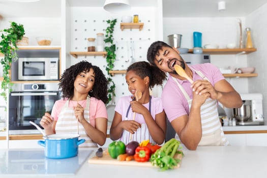 Playful African American Family Having Fun In Kitchen, Singing And Dancing While Cooking Lunch At Home, Cheerful Family With Daugther Using Spatulas As Microphones, Free Space photo