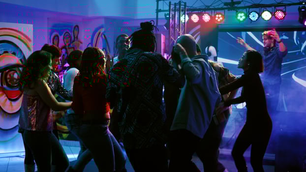 Diverse people having fun partying at club, dancing on live music performance with colorful glowing lights. Young men and women enjoying disco party, social gathering. Handheld shot. photo