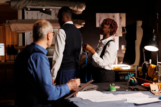 African american gentleman getting measurements taken by professional suitmakers in dark studio workspace. Masterful tailors looking for ideal client proportions for upcoming custom made suit photo