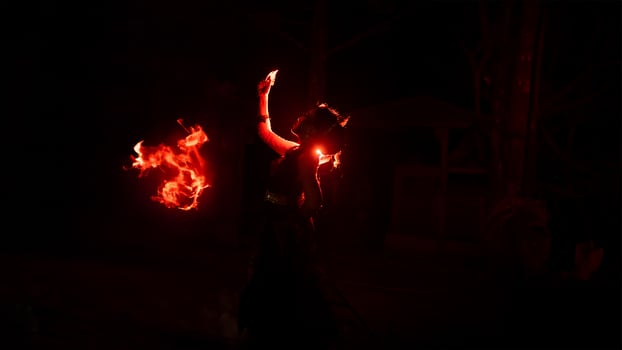 The silhouette of a female dancer holding jewelry in the dark of night is lit by the light of a burning fire photo