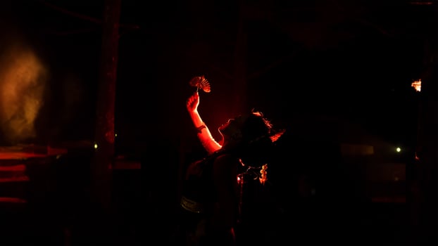 The silhouette of a female dancer holding jewelry in the dark of night is lit by the light of a burning fire photo