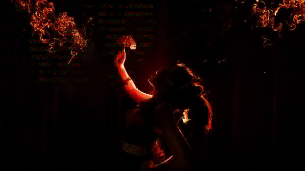the silhouette of a female dancer holding sparkling jewelry and looking sharp in the dark with fire burning in the background photo