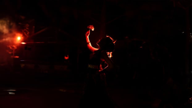 the silhouette of a female dancer holding jewelry shines brightly around the flames and looks bold in the dark photo