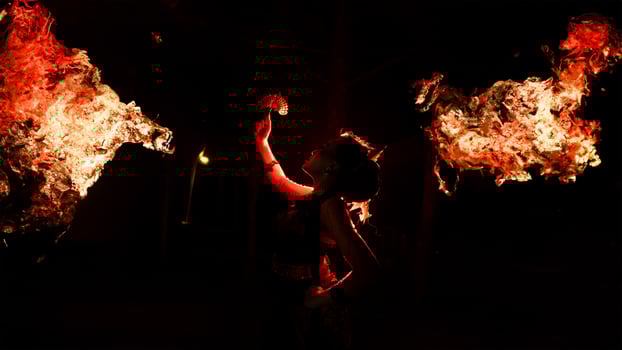 the silhouette of a female dancer holding jewelry shines brightly around the flames and looks bold in the dark photo
