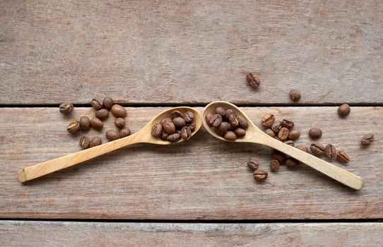 Roasted coffee beans in wooden spoon and spread on wooden table background. It is a medium roast with medium intensity coffee flavor. Slightly sweet and sour, suitable for both hot and cold coffee. photo