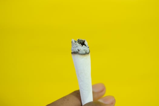 A man hand holds a handmade cigarette on yellow background photo