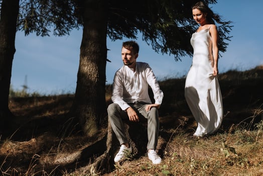 Stylish model couple in the mountains in summer. A young girl in a white silk dress walks along the slope against the background of the forest and mountain peaks. photo
