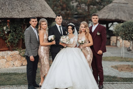 Front view of newlyweds standing and hugging, between friends. Girls in golden dresses hold bouquets, the bride in a voluminous dress, the groom and his friends in suits. Wedding in nature photo
