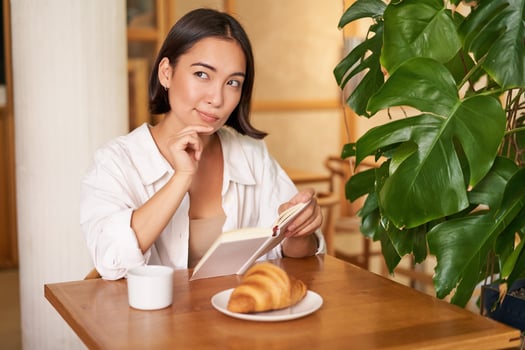 Smiling beautiful girl with a book, reading with thoughtful smirk, thinking of something, drinking coffee in cafe photo