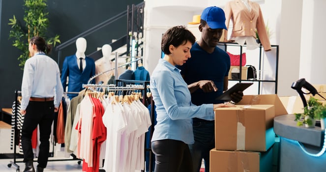 Store employees checking cardboard boxes, analyzing shipping report on tablet computer in shopping centre. Manager working at online customers orders, preparing packages for courier in modern boutique photo