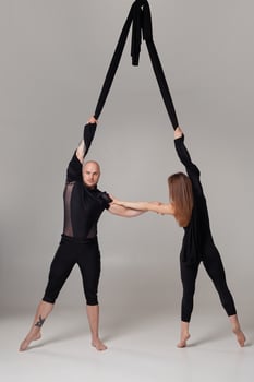 Beautiful girl and an athletic man in a black sport suits are performing an acrobatic elements in a studio. photo