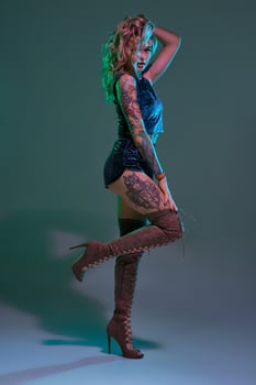 Attractive young blonde girl in blue velour booty shorts and maroon suede high boots posing on camera in studio photo