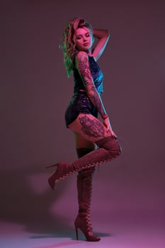 Attractive young blonde girl in blue velour booty shorts and maroon suede high boots posing on camera in studio photo