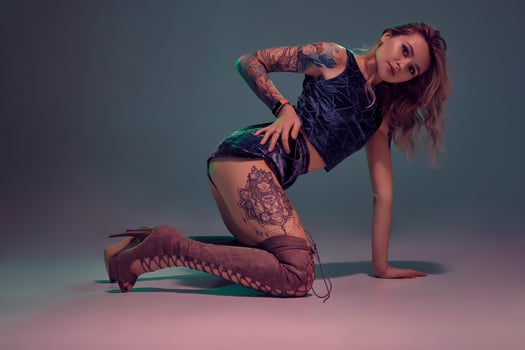 Attractive young blonde girl in blue velour booty shorts and maroon suede high boots posing on camera in studio photo