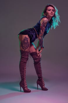Attractive young blonde girl in blue velour booty shorts and maroon suede high boots posing on camera in studio photo