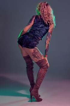 Attractive young blonde girl in blue velour booty shorts and maroon suede high boots posing on camera in studio photo