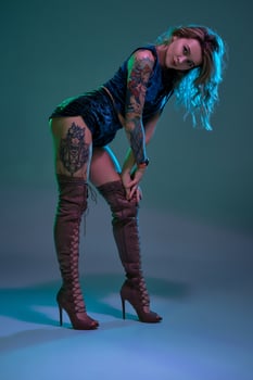 Attractive young blonde girl in blue velour booty shorts and maroon suede high boots posing on camera in studio photo