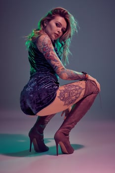 Attractive young blonde girl in blue velour booty shorts and maroon suede high boots posing on camera in studio photo